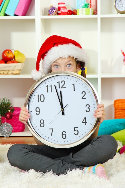 Niña sosteniendo el reloj cerca del árbol de navidad