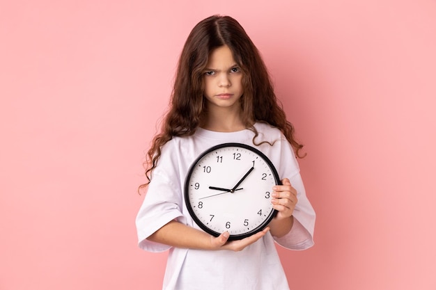 Niña sosteniendo un reloj de pared siendo infeliz la fecha límite está triste por no haber terminado su tarea a tiempo