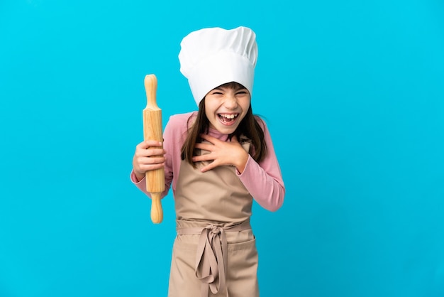 Niña sosteniendo un rodillo aislado en la pared azul sonriendo mucho