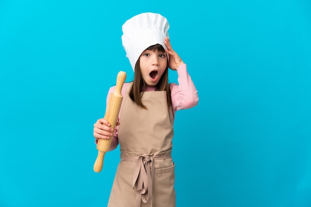 Niña sosteniendo un rodillo aislado sobre fondo azul con expresión de sorpresa