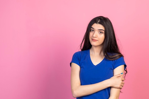 Niña sosteniendo su mano en su brazo y de pie sobre fondo rosa