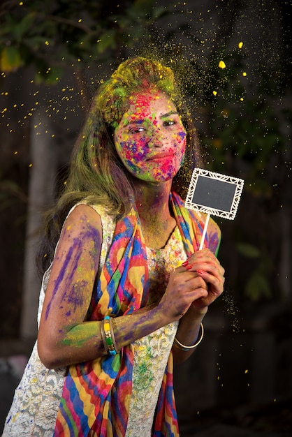 Niña sosteniendo el tablero pequeño con motivo del festival de Holi con caras pintadas con colores empolvados, con un toque de color.