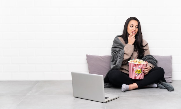 Niña sosteniendo un tazón de palomitas de maíz y mostrando una película en una computadora portátil nervioso y asustado