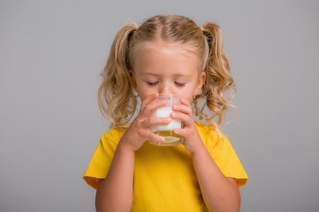 Niña sosteniendo un vaso de leche sobre un fondo claro, espacio para texto