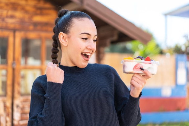 Una niña sosteniendo un yogur y un plato de frutas.