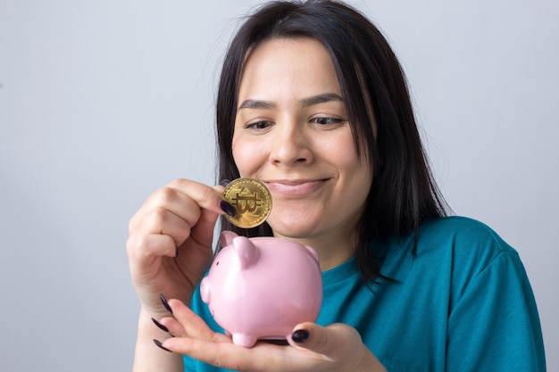 La niña sostiene una alcancía rosa y una moneda en sus manos. El concepto de riqueza y acumulación.