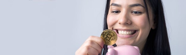 La niña sostiene una alcancía rosa y una moneda en sus manos. El concepto de riqueza y acumulación.