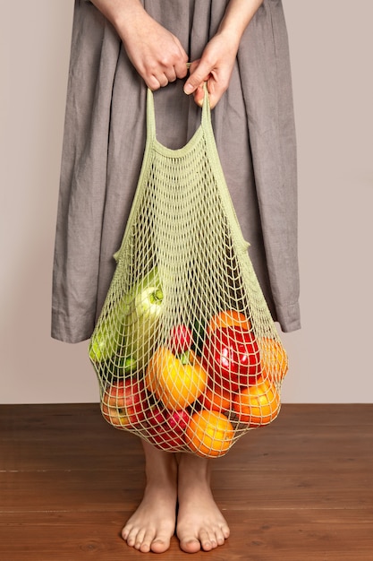 Foto niña sostiene una bolsa de cadena con frutas y verduras. el concepto de compras ecológicas y buena nutrición. entrega de productos. protección del medio ambiente.