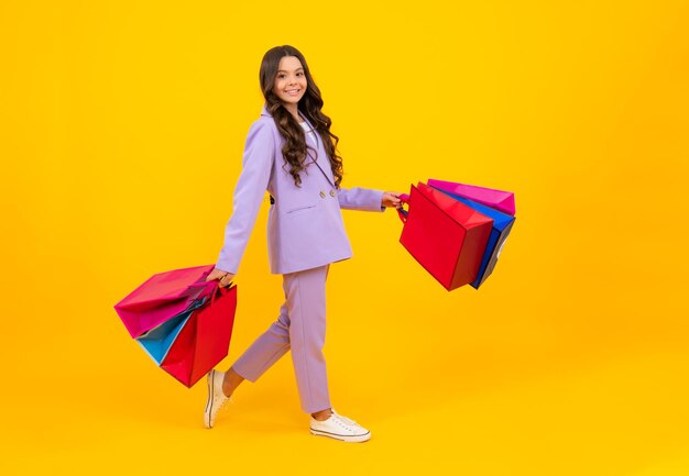 Niña sostiene una bolsa de compras disfrutando de la venta aislada en un fondo amarillo Retrato de una adolescente lista para ir de compras