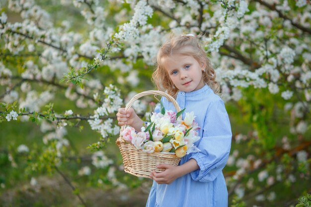 Una niña sostiene una canasta de flores cerca de un árbol en flor