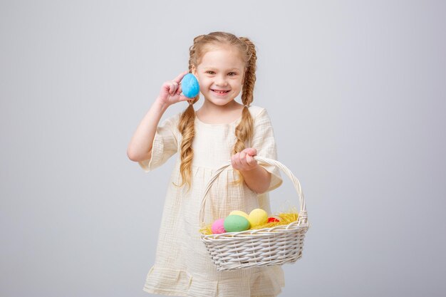 Una niña sostiene una canasta con huevos de Pascua en un fondo blanco aislado