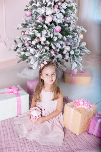 Niña sostiene carrusel de juguetes musicales cerca del árbol de Navidad