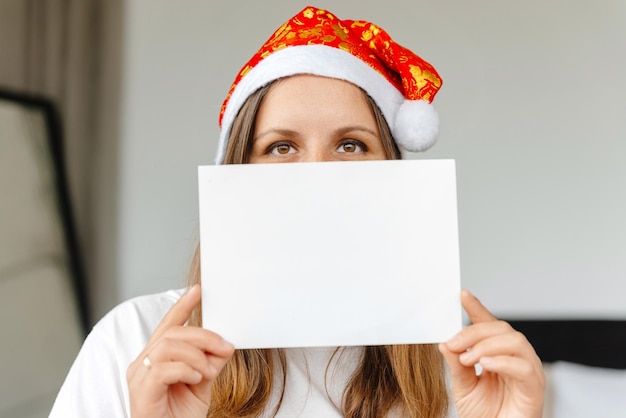 Una niña sostiene una carta en blanco a una mujer de santa claus con un sombrero de navidad que sostiene una carta delante o