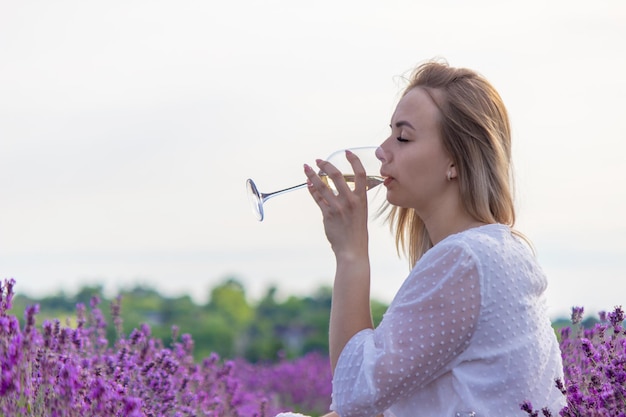 Una niña sostiene una copa de vino blanco contra el fondo de un campo de lavanda Una niña bebe vino en un campo de lavanda