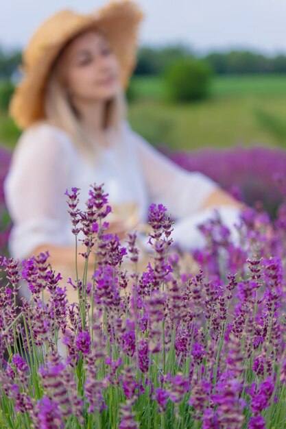 Una niña sostiene una copa de vino blanco contra el fondo de un campo de lavanda Una niña bebe vino en un campo de lavanda