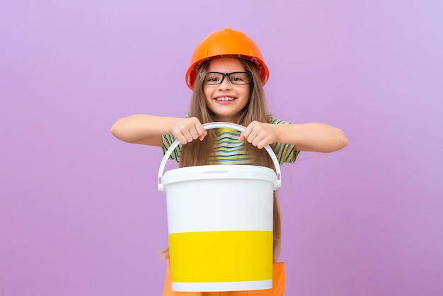 Foto una niña sostiene un cubo de pintura en sus manos y va a hacer reparaciones en el baño.