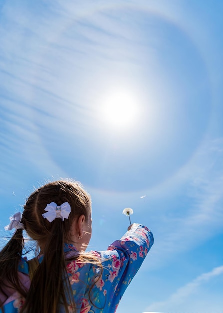 Una niña sostiene un diente de león al sol.