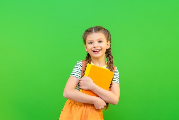 Una niña sostiene dos libros en sus manos y sonríe. Una colegiala con libros sobre un fondo verde aislado.