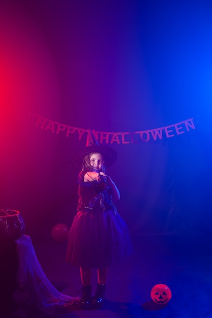 La niña sostiene la escoba en la fiesta de Halloween. Niño niña usa disfraz de bruja. Concepto de fantasía, cuento de hadas y mascarada.