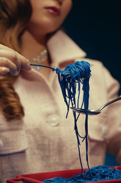 Foto la niña sostiene espaguetis azules en un tenedor sosteniéndolos con una cuchara