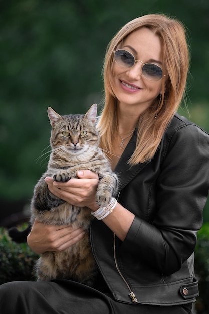 La niña sostiene un gato en sus brazos contra el telón de fondo de la naturaleza en el parque el gato mira a la cámara
