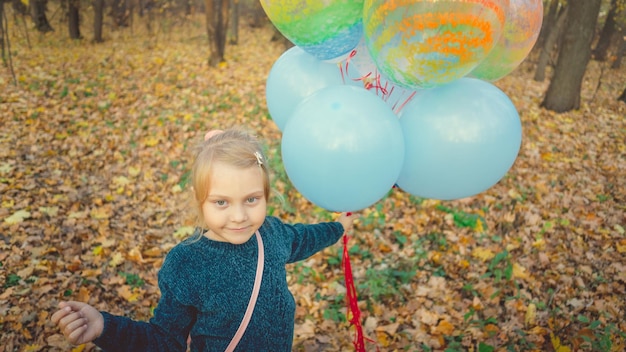 Una niña sostiene globos en un paseo por el bosque de otoño