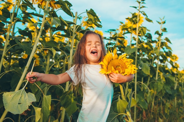 Una niña sostiene un gran girasol floreciente. Pétalos de girasol amarillo. Un fondo natural asociado al verano. preparándose para la cosecha