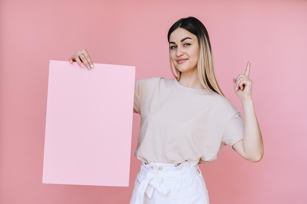 Foto la niña sostiene una hoja de papel rosa en la mano derecha y el dedo índice apunta hacia arriba con la mano izquierda.