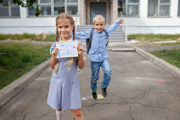 La niña sostiene la imagen con el mensaje de regreso a la escuela y el niño con mochila corre después del primer día sin conexión