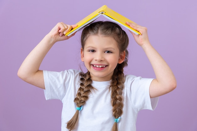 Una niña sostiene un libro como un techo sobre su cabeza sobre un fondo púrpura