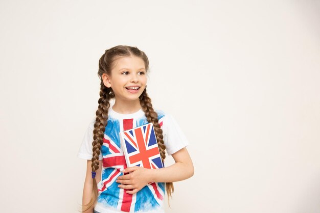 Una niña sostiene un libro de inglés con la bandera de Gran Bretaña en su camiseta Cursos de inglés para niños