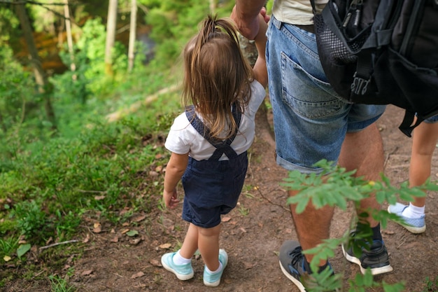 La niña sostiene la mano de su padre al borde de un hueco del bosque.