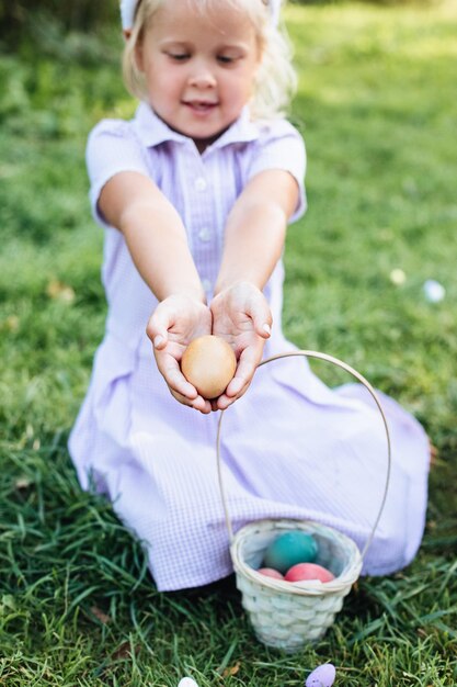 Una niña sostiene en las manos huevos de Pascua cerca de un busket de mimbre en un césped contra un fondo verde borroso Concepto de vacaciones de primavera