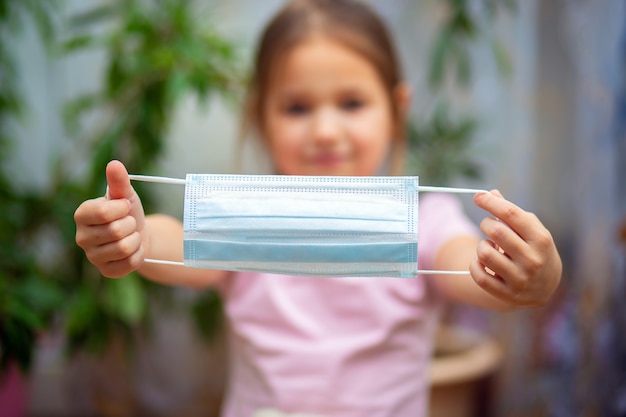 La niña sostiene una máscara médica en manos extendidas. El niño se pone una máscara protectora