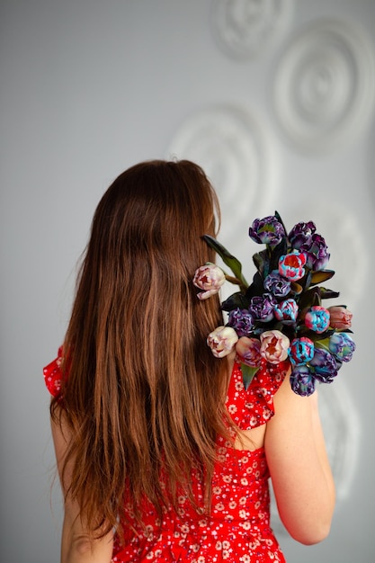 Una niña sostiene muchos tulipanes en sus manos en el Día de la Mujer Vestido rojo hermoso cabello largo