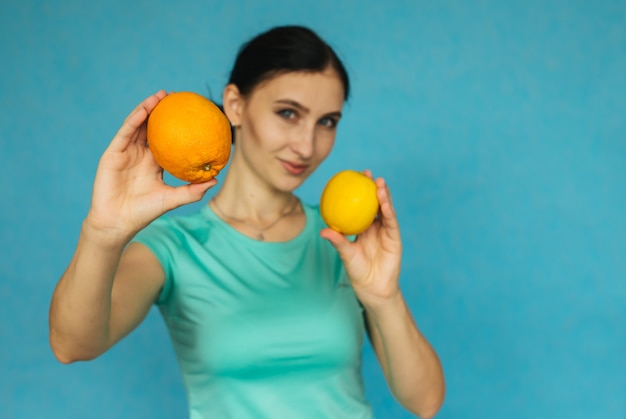 Una niña sostiene una naranja y un limón. Niña sobre un fondo azul.