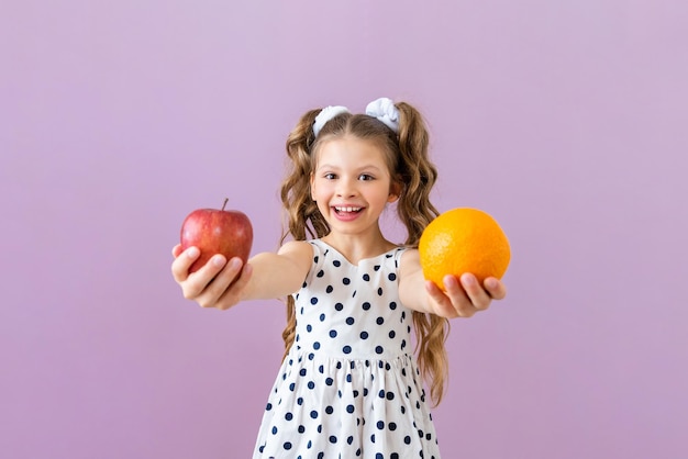 Una niña sostiene una naranja y una manzana Vitaminas para niños y escolares