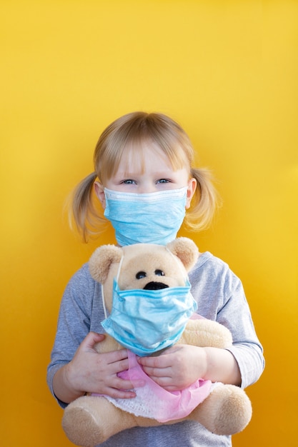 La niña sostiene un oso de peluche tanto en máscara médica.