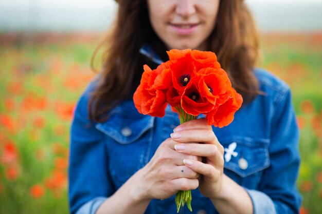 Una niña sostiene un ramo de hermosas amapolas rojas en su mano frente a ella. De cerca.