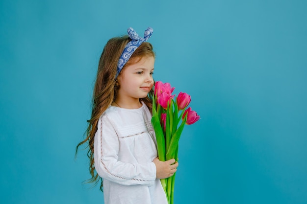 Una niña sostiene un ramo de tulipanes rosas sobre un fondo azul.