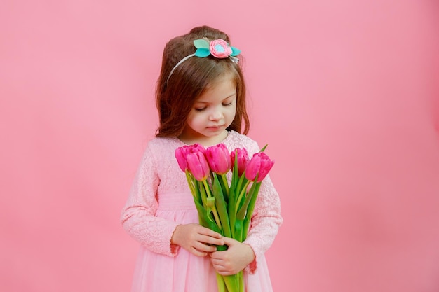 Una niña sostiene un ramo de tulipanes rosas sobre un fondo rosa