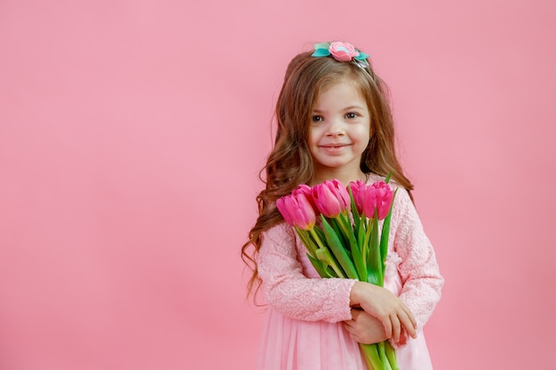 Niña sostiene un ramo de tulipanes sobre un fondo rosa