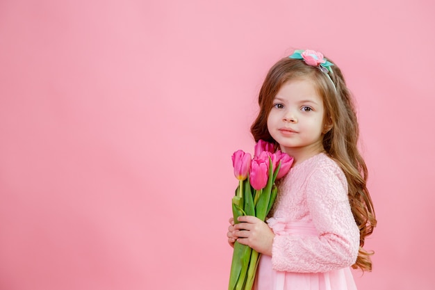 Niña sostiene un ramo de tulipanes sobre un fondo rosa