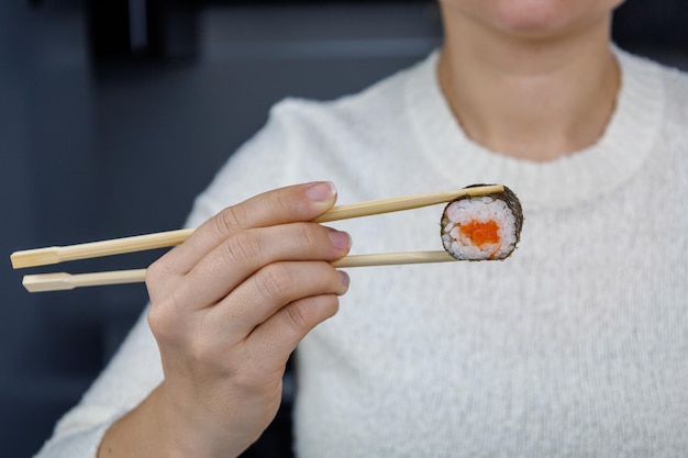 Una niña sostiene un rollo con pescado rojo en la mano con palillos en la cocina