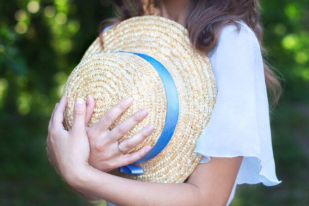 Una niña sostiene un sombrero de paja con una cinta azul en sus manos en un día de verano.