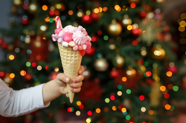 La niña sostiene en su mano un cono de waffle lleno de malvaviscos rosas y dulces