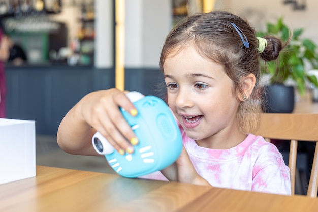 Una niña sostiene en sus manos una cámara digital de juguete azul para niños para la impresión instantánea de fotografías.