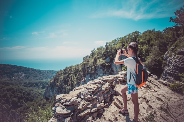 Una niña sostiene un teléfono inteligente para tomar fotografías de un hermoso paisaje de montaña