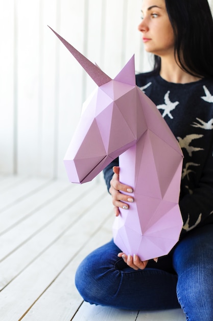Foto la niña sostiene un unicornio rosa modelo de unicornio 3d en el alféizar de la ventana. ilustraciones