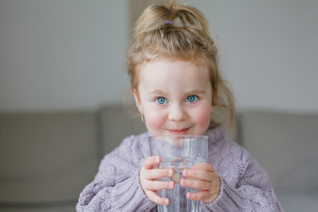 Una niña sostiene un vaso de agua, bebe. Acogedor.